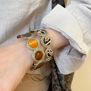 Close-up of retro leopard print and amber round charms on vintage woven metal bracelets