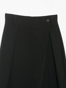 Detailed close-up of high-waist asymmetric black trousers with button and belt loop features