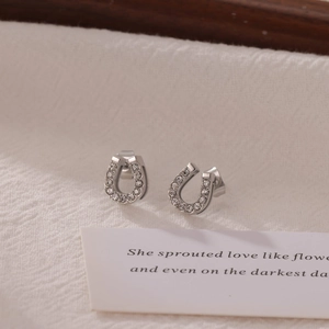 Sparkling silver horseshoe earrings with crystal paving on minimalist cream background