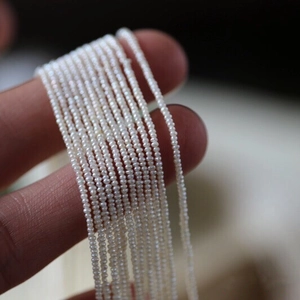 Macro shot of ultra-fine tiny white natural pearls on a string held by a hand