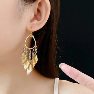 Détail de boucles d'oreilles à pampilles dorées avec perles grises sur un modèle