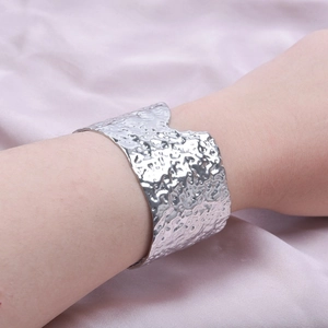 Detailed view of silver wide cuff bracelet with hammered texture on silk fabric