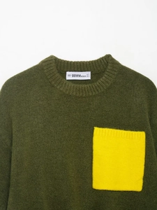 Gros plan du pull en maille vert foncé avec col rond et poche jaune contrastée