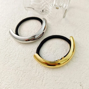 Minimalist C-shaped metallic hair ties in gold and silver finish on textured surface
