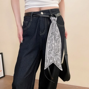 Détail d'une ceinture en cuir noir avec foulard en soie paisley sur un jean bleu