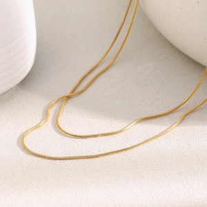 Detail view of gold double layer necklace on minimalist beige textured surface