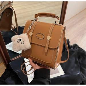 Close-up of brown faux leather backpack with white stitching and plush bear charm