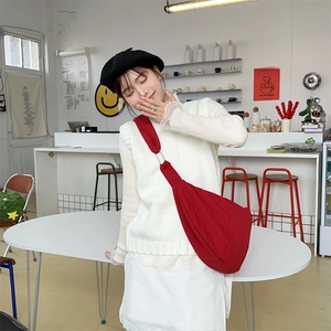 Close-up of a red nylon dumpling crossbody bag styled with a white knit sweater and beret