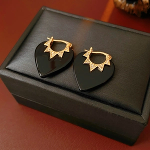 Close-up of black heart earrings with gold star zircon detail on a jewelry box