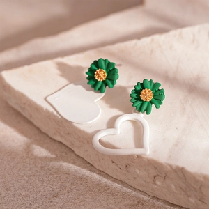 Detail of asymmetrical green daisy and white acrylic heart earrings on white stone