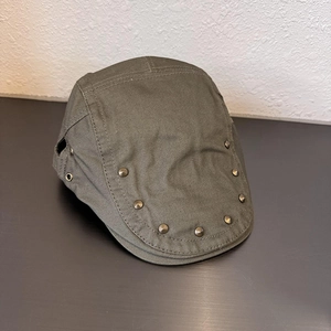 Close-up of olive green cotton twill flat cap featuring metallic rivet details and side eyelets