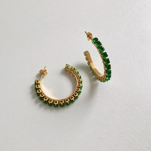 Détail de boucles d'oreilles en C dorées avec incrustations de zircons verts carrés