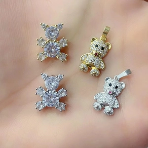 Macro view of crystal-encrusted teddy bear pendants in gold and silver on a palm