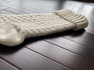 Close-up of cream knitted Christmas stocking with textured patterns on dark wood floor