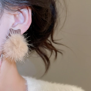 Close-up of a model wearing soft beige pompom earrings with elegant furry texture