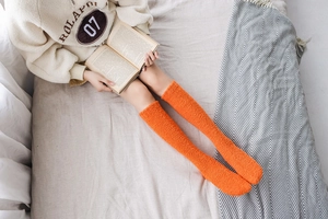 Close-up of orange coral fleece knee-high socks worn in a cozy home reading setting