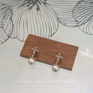 Vue détaillée d'une boucle d'oreille croix en argent avec perle sur un bloc en noyer