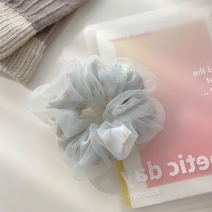 Close-up of light blue mesh hair scrunchie with yellow daisy floral pattern on a desk