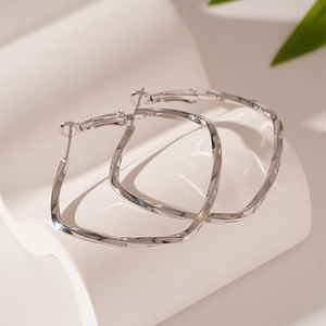 Detailed view of silver twisted geometric hoop earrings on a minimalist white display