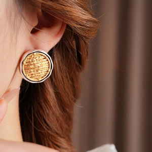 Close-up of circular earrings with woven texture in gold and silver finish on model