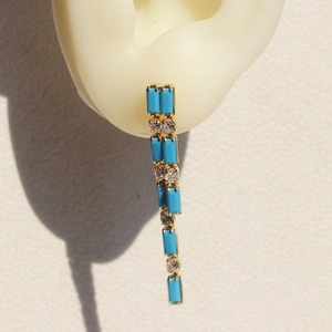 Detail of gold tassel earrings with turquoise and cubic zirconia on a model ear