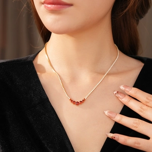 Detail view of gold necklace with red zircon pendant worn on a model neckline