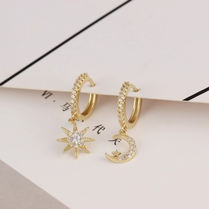 Detail of gold-plated hoop earrings featuring asymmetric cubic zirconia star and moon charms