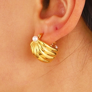 Close-up of a gold shell-textured earring with a white pearl on the model's ear
