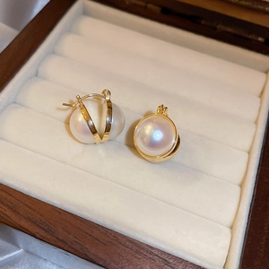 Close-up of golden V-shaped pearl earrings on a premium brown wooden jewelry box