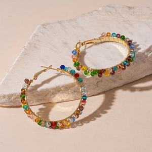 Close-up of rainbow crystal beads on gold hoop earrings atop a textured natural stone
