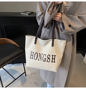 Close-up of a large canvas tote bag with letter prints and contrasting straps