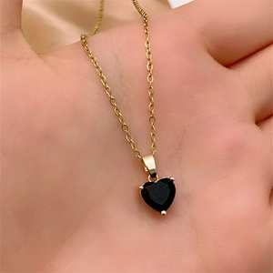 Close-up of a gold heart necklace with black zircon held in hand for size display