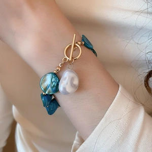 Detail of a beach-style gold OT buckle bracelet with teal beads and white shell accents