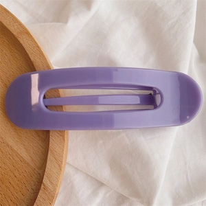 Close-up of a minimalist matte purple rectangular hair clip on a wooden tray background