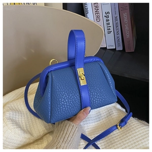 Close-up of blue pebbled leather handbag with gold twist lock held in a lifestyle setting