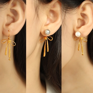 Elegant gold bow earrings with white and grey pearls shown in multiple wearing angles