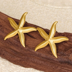 Detailed close-up of 18k gold starfish stud earrings on a rustic wood and sand background
