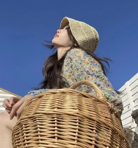 Detail of beige crochet bucket hat with colorful knit sweater against a clear blue sky background