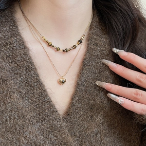 Close-up of double-layered gold necklace with heart pendant and brown tiger eye beads