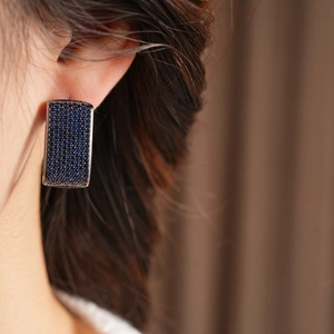 Close-up of vintage-style rectangular blue zircon huggie earrings worn on model's ear
