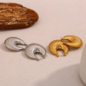 Detailed view of hollow ram horn earrings in polished 18K gold and silver finishes