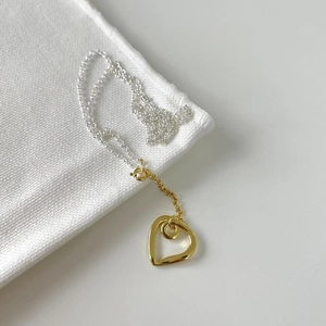 Macro shot of minimalist silver heart necklace with gold bicolor chain on fabric