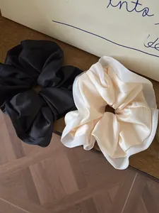 Detail of premium black and cream satin scrunchies with sheer trim on wooden surface