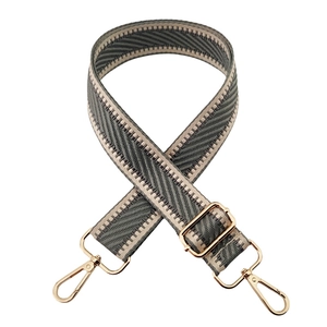 Close-up of grey and white diagonal striped bag strap with gold metal hooks and buckle