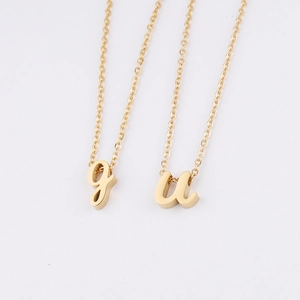 Détails des pendentifs lettres 'g' et 'u' en minuscules dorées sur chaînes d'acier