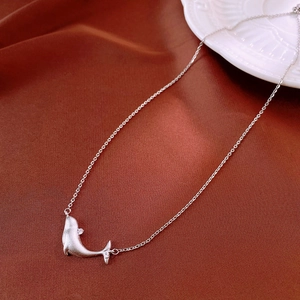 Detailed macro view of a silver dolphin pendant with matte texture on silk fabric