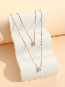 Detail of layered gold-tone chains with elegant pear-shaped zircon pendants on white stand