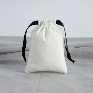 Detail of white cotton jewelry pouch with black ribbon drawstring on gray fabric