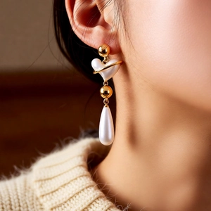 Macro shot of vintage gold heart earrings with drop pearls worn by a female model