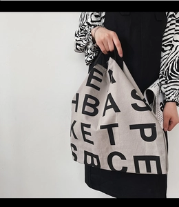 Lifestyle view of large cream canvas tote bag with bold black letter prints on model